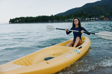 Obraz premium A lone kayaker paddles a bright yellow kayak along a calm shoreline, capturing a moment of adventure, focus, and connection with water and sky.