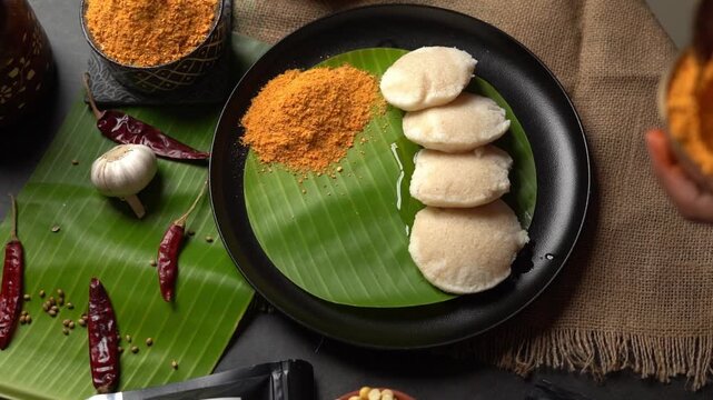 Soft idli plated with milagai podi and chutney on a banana leaf