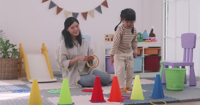 Happy Asian mother and daughter playing a colorful ring toss game together indoors.