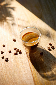 Fresh espresso coffee in a double wall glass cup illuminated by warm morning sunlight on a rustic wooden table.
