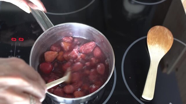 A woman is making strawberry jam in her kitchen. She is making the jam on an induction hob.