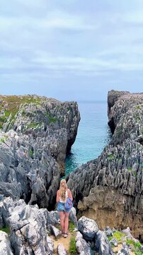 Woman hiker standing on sharp rocks looking at a narrow sea canyon on the coast of asturias spain