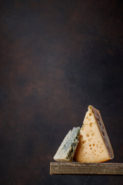 Cheese pieces on rustic wooden table dark background
