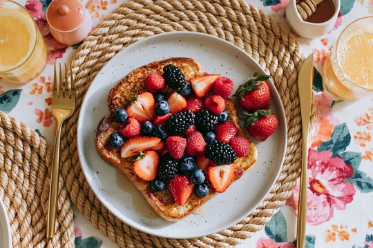 Overhead shot of a summer brunch table featuring a plate of French toast topped with mixed berries, surrounded by drinks and decorative tableware