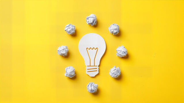Creative paper light bulb icon surrounded by small crumpled paper balls on yellow background representing bright idea brainstorming innovation and problem solving concept.