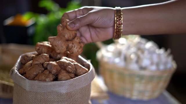 Hands selecting dried ginger beside a basket of garlic bulbs