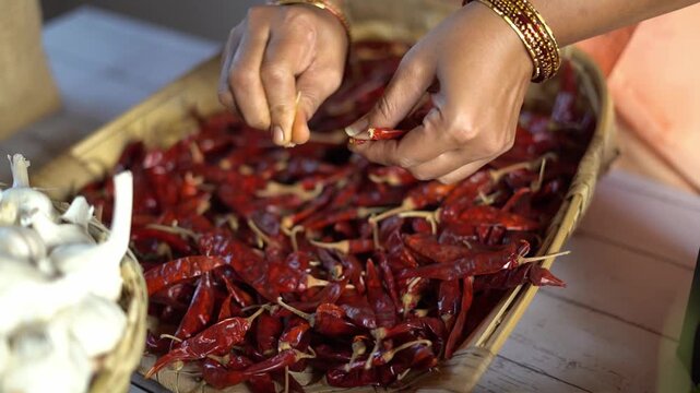 Close up of hands destemming dried red chillies before grinding