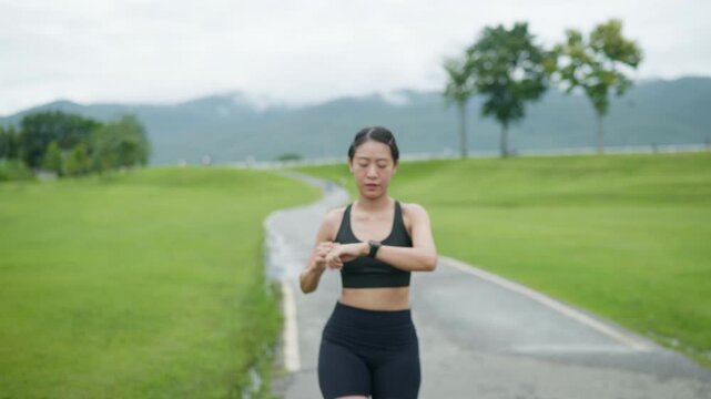 Female runner checking a smartwatch after running on a park track, representing fitness tracking, healthy lifestyle, exercise routine, wellness and longevity concept.