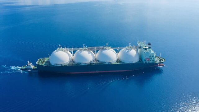 Aerial view of a large liquefied natural gas tanker ship sailing on calm blue ocean water with a tugboat assisting
