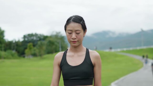 Female runner checking a smartwatch while cooling down after jogging on a park path, representing fitness tracking, recovery routine, healthy lifestyle, wellness and longevity concept.