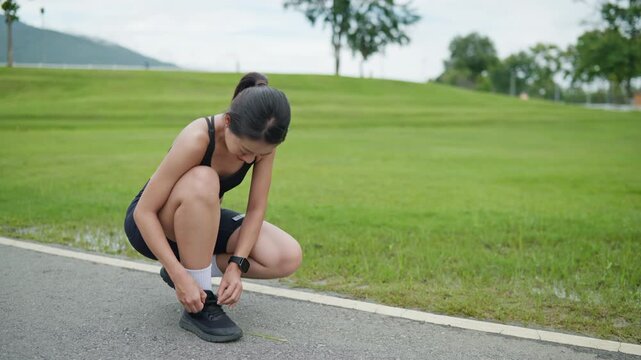 Female runner tying shoelaces before running in a public park, representing workout preparation, fitness routine, healthy lifestyle, safety, wellness and active living concept.