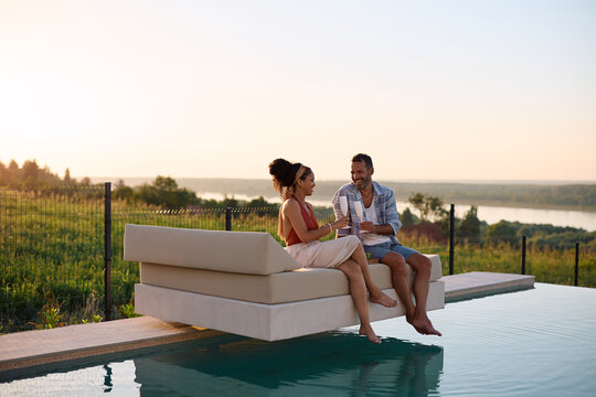 Happy couple toasting while drinking champagne by the pool on summer sunset.