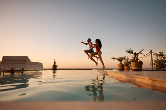 Carefree couple jumping into infinity pool at summer sunset.