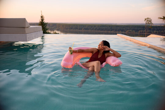 Happy black woman enjoying in the swimming pool at sunset.