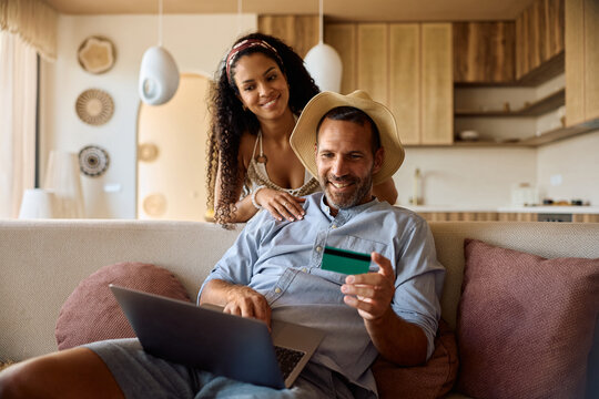 Happy couple of travelers paying online with credit card and laptop.