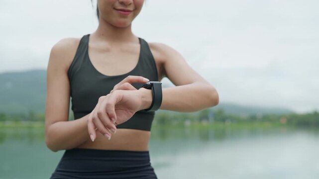Woman runner adjusting smartwatch settings before exercise in a public park, representing workout preparation, wearable technology, healthy lifestyle, personal health and wellness concept.