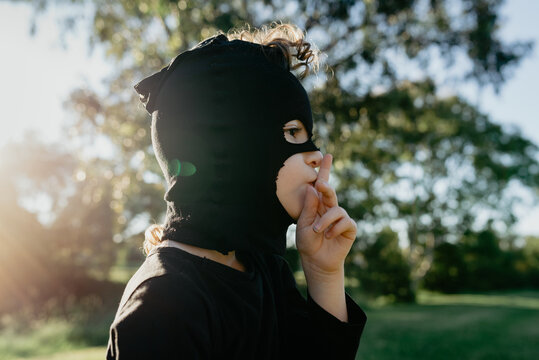 Silent Ninja. Profile portrait of a happy, confident young boy with curly hair dressed up in a black Ninja costume wearing a mask handmade from his mum's black panty hose stockings; Australia