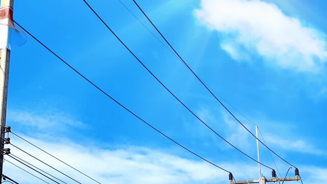 Electric poles and high-voltage power lines contrast against the bright blue sky. This upward-facing view conveys the message of infrastructure, power transmission systems, energy, technology, and urb