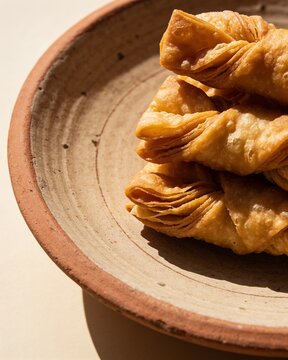 Traditional crispy fried dough twists pastry served in a rustic terracotta bowl under warm natural sunlight, classic sweet or savory Asian snack.
