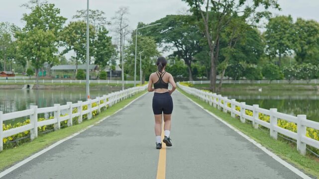 Woman warming up with light jogging by a reservoir road, showing outdoor fitness, healthy lifestyle, movement preparation and longevity concept.