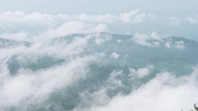 Thick mist hangs over the mountains; heading toward a wooded hill in the Catalan region, one can see fog drifting over the lush green forest during the rainy season.