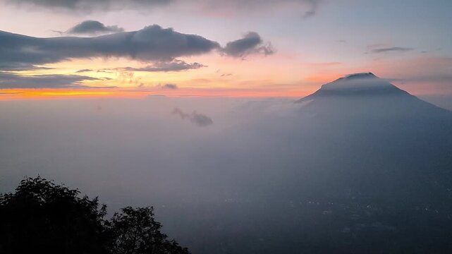 Scenic sunrise over Mount Sumbing with misty volcanic clouds, viewed from the Mount Sindoro hiking trail in Central Java, Indonesia, showcasing a peaceful tropical mountain landscape.