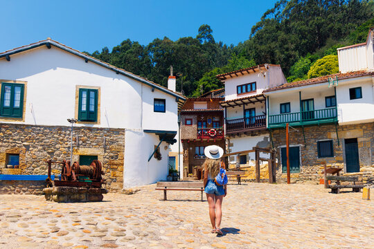 Woman tourist with backpack walking on cobbled square in historic village of Tazones, discovery of Asturias in Spain