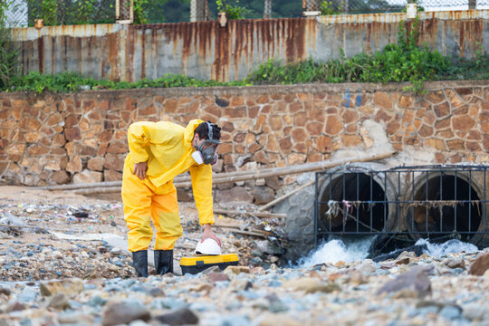 Environmental scientist in hazmat suit inspecting polluted water discharge, Toxic waste inspector in protective hazmat gear checking water quality near industrial drainage