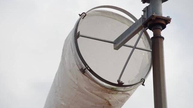 Close view of a windsock at a remote aerodrome gently moving in a light breeze against blue sky and passing clouds. Aviation, weather conditions and rural airstrip concept