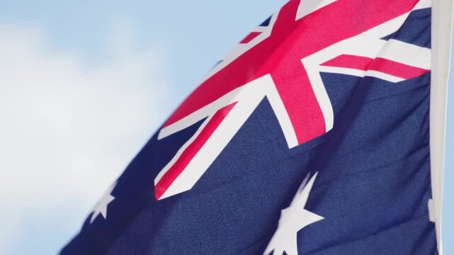 Close up of the Australian National Flag flying on a flagpole against a clear blue sky. Symbol of Australian identity, culture, heritage and recognition in Australia
