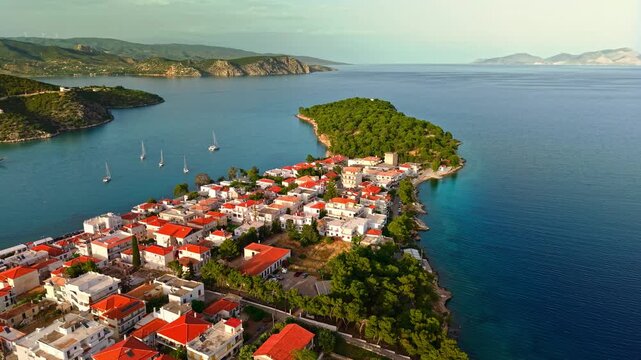 Panoramic aerial view of Ermioni, Greece, capturing the coastal peninsula in warm evening light and clear blue waters stretching into the horizon