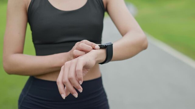 Woman runner adjusting smartwatch settings before exercise in a public park, representing workout preparation, wearable technology, healthy lifestyle, personal health and wellness concept.