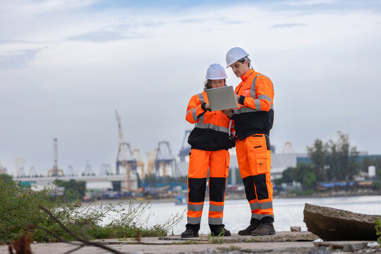 Engineers in safety gear using laptop at shipping port, Industrial engineers team discussing project work on laptop at harbor, Construction project managers inspecting shipping terminal site