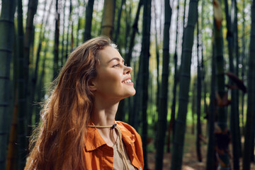 Woman smile in bamboo forest with nature sunlight on her face, profile portrait of a redhead in an orange jacket enjoying peaceful outdoors, relaxation and joyful serenity. © SHOTPRIME STUDIO