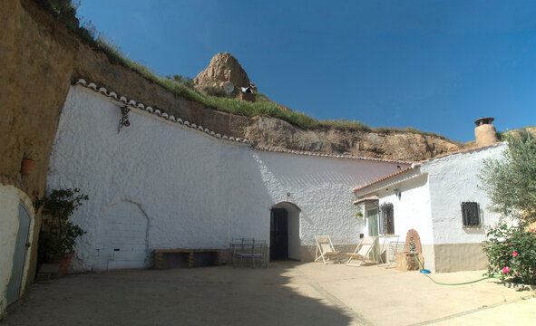 Traditional white troglodyte cave house facade with courtyard and chimneys carved in tuff rocks in Guadix, Spain