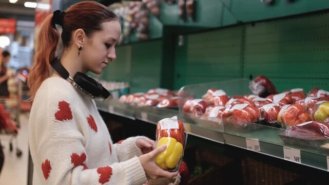 A young woman in a white wool sweater buys fruits at a supermarket in winter.