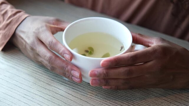 Women's hands hold a mug of hot tea in the morning during the cold season. A young woman warms her hands on a very hot cup of tea.