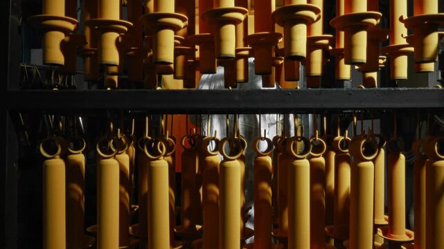 Powder-coated cylindrical automotive components hanging from overhead conveyor racks inside industrial finishing line under warm directional lighting, with powder, coating, automotive, component