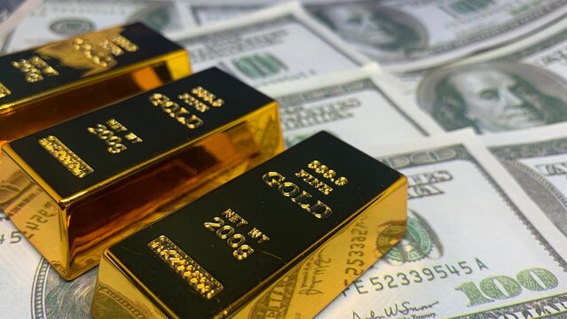 Stacked gold bars arranged on scattered one-hundred-dollar bills, illustrating asset accumulation and diversified financial holdings