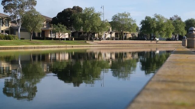 Tree-lined homes reflect on a still waterway at Sanctuary Lakes, Point Cook. Tranquil waterside living and desirable environment in suburban Melbourne, Australia.