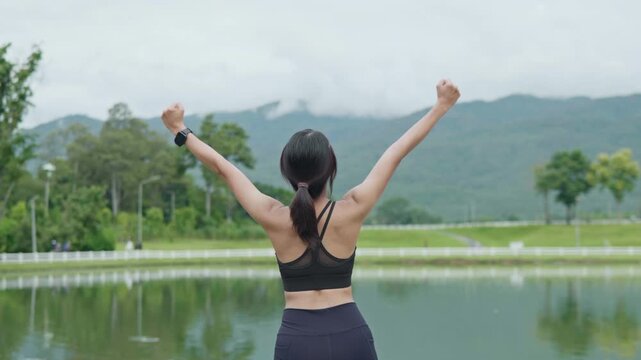 Female runner celebrating with happiness after outdoor exercise by a scenic lake, representing fitness achievement, healthy lifestyle, wellness and longevity.