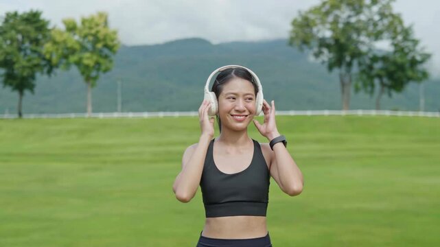 Female runner wearing headphones and listening to music outdoors in a park, representing fitness lifestyle, relaxation, wellness, motivation and active living.