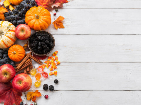 Composici&oacute;n de frutas y elementos de oto&ntilde;o en una mesa de madera blanca con calabazas y especias