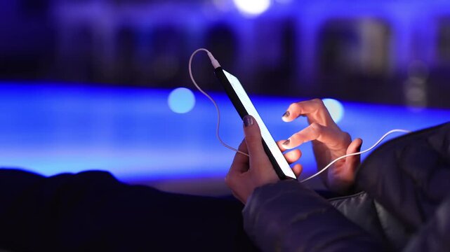 Woman using smartphone by pool at night &ndash; glowing screen, copy space, modern lifestyle.