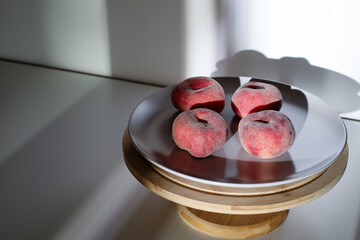 Four ripe saturn peaches on a plate placed on a wooden stand. High contrast dramatic shadows on a white background. ©  Tsvyk L.