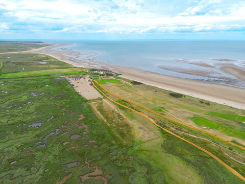 Dramatic drone view of the popular Norfolk, UK beach of Brancaster seen at low tide. The expansive beach can be seen tougher with a Golf Course and Club in the centre of the image.