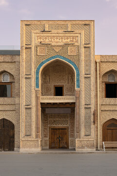 Old building close Poi Kalyn square in Bukhara with intricate brickwork and turquoise tile arch at dusk. Ideal for travel publications, heritage brochures, and cultural media about Central Asia.
