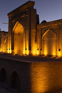 Historic brick portal with pointed arches illuminated at twilight in Ichan Kala old town of Khiva, Uzbekistan. Warm golden uplighting contrasts with deep blue evening sky, ideal for travel, heritage.