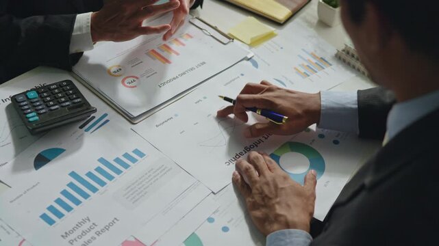 Top view of coworkers reviewing and presenting business reports with charts and graph documents on the desk, showing teamwork, collaboration, planning and financial analysis.