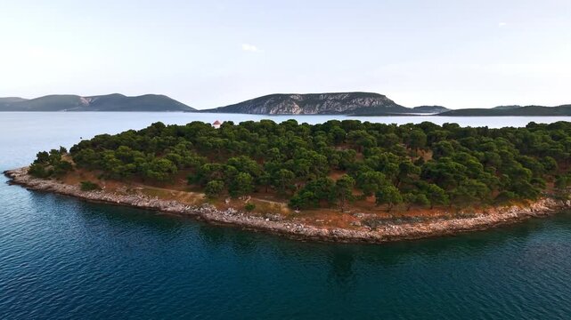 Aerial orbit around the pine-covered Ermioni peninsula in Greece during golden evening light